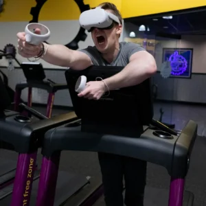 An adult engaging in virtual reality exercise on a treadmill, with VR goggles and controllers.