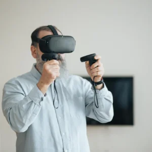 Senior man exploring virtual reality with VR headset and controllers indoors.