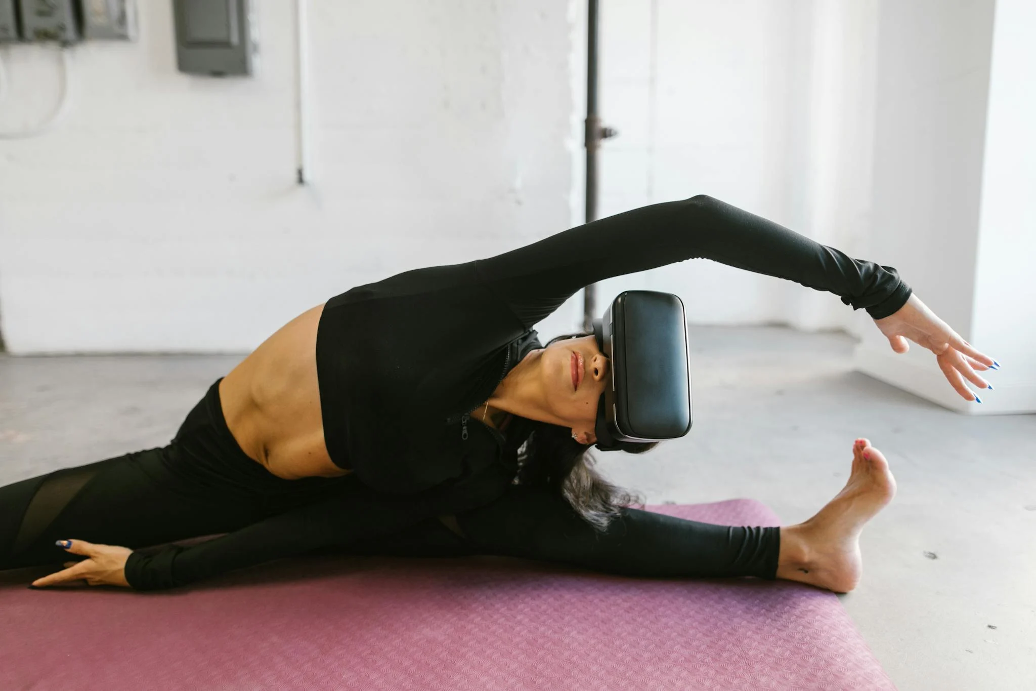 Woman in activewear using VR goggles for yoga stretching on a mat indoors.